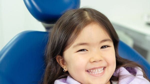 Young girl grinning in a blue dental chair at a check on the best age for braces