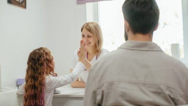 Young girl high-fiving her clinician at a dental visit, the first check where braces at age 7 come up