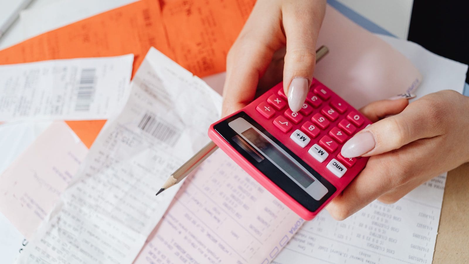 Hand using a pink calculator over a pile of bills to work out how much braces cost