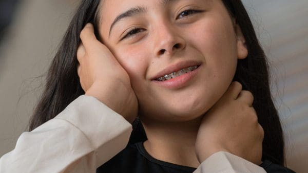 Teen girl with braces holding her cheeks, the sore feeling after braces tightening