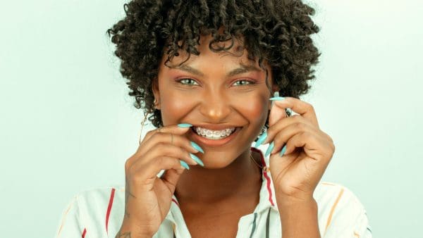 Young woman with braces touching her teeth, where braces wax covers a bracket that rubs