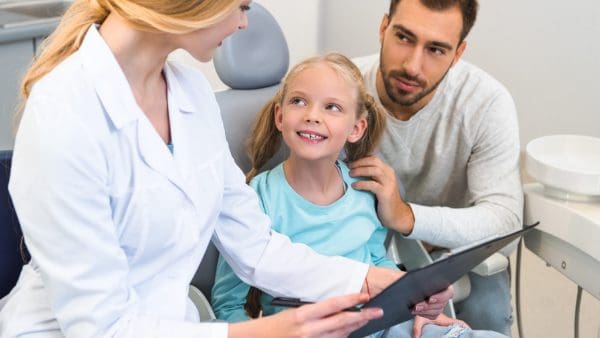 Girl in the dental chair with her dad as the orthodontist reviews her chart, choosing the best orthodontist