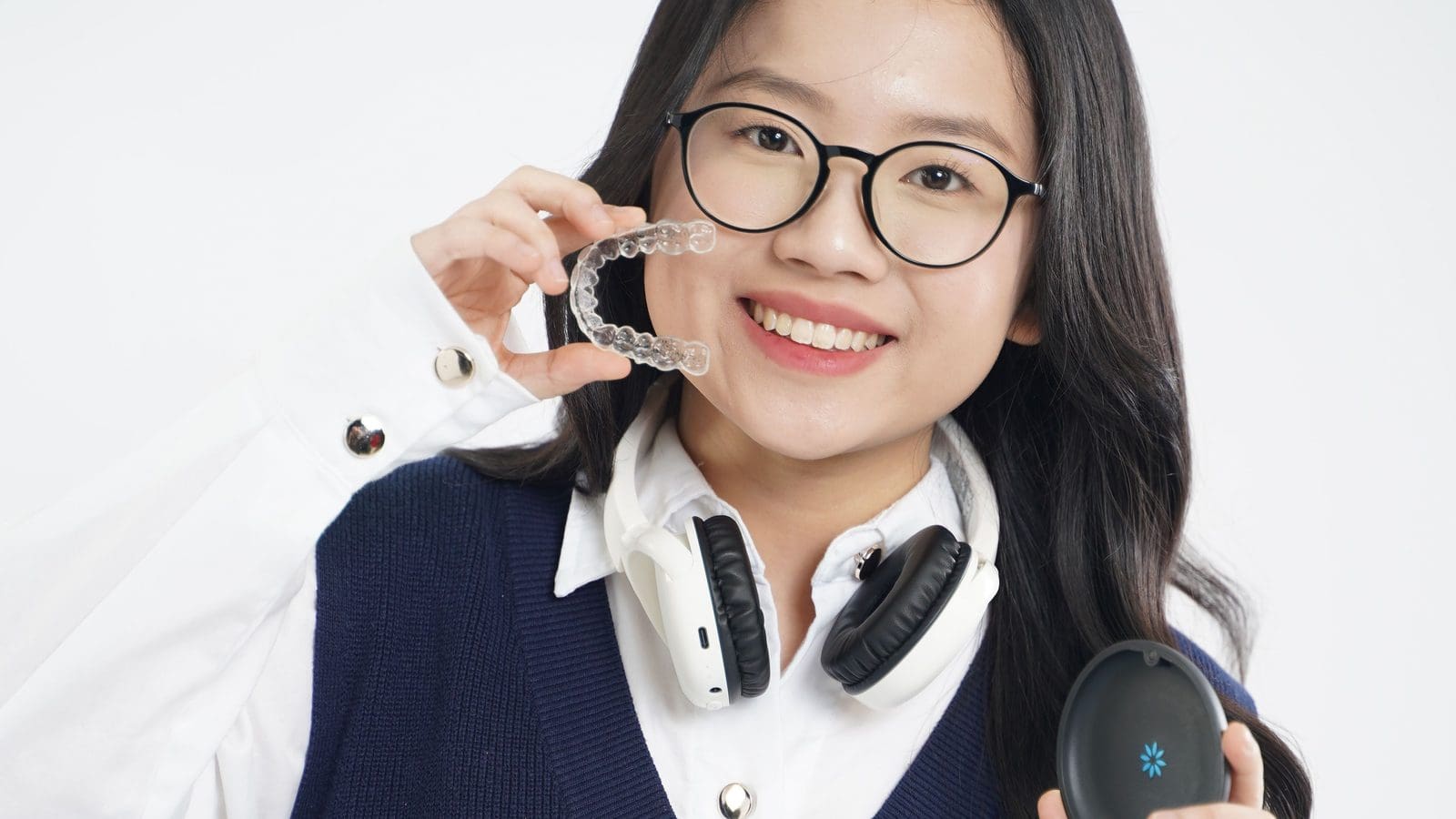 Smiling young woman in glasses holding a clear aligner and its case, comparing clear aligners vs braces