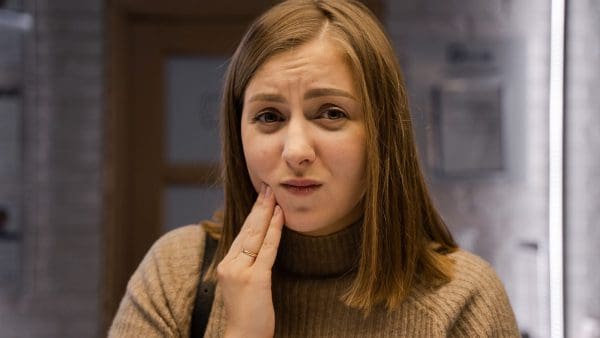 Woman pressing a hand to her sore jaw, the feeling behind the question do braces hurt