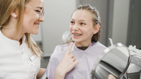 Smiling teen with braces talking with her dentist at a checkup, where orthodontist vs dentist roles differ