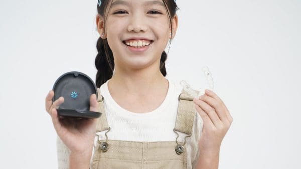 Smiling girl holding a clear retainer and its case, the retainer replacement many patients need