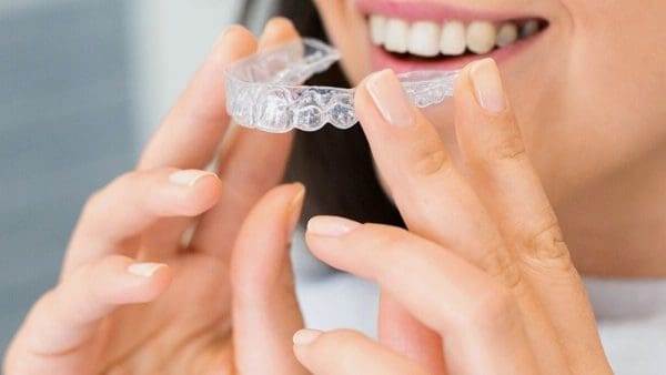 Woman holding up a clear retainer tray, the appliance behind the cost of a new retainer