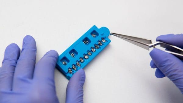 Tweezers lifting a bracket from a bracket tray, the hardware used for self ligating braces