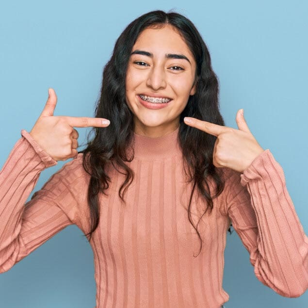 Tooth by Tooth Teen showing off braces with confident smile, wearing pink sweater against blue background