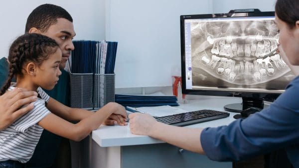 Parent and daughter looking at a dental X-ray with the doctor, deciding when to see an orthodontist